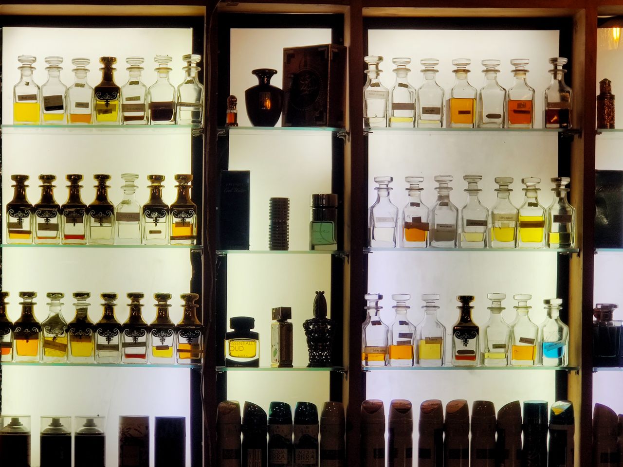 team-01 Aesthetic arrangement of diverse perfume bottles on illuminated shelves showcasing luxury fragrances.