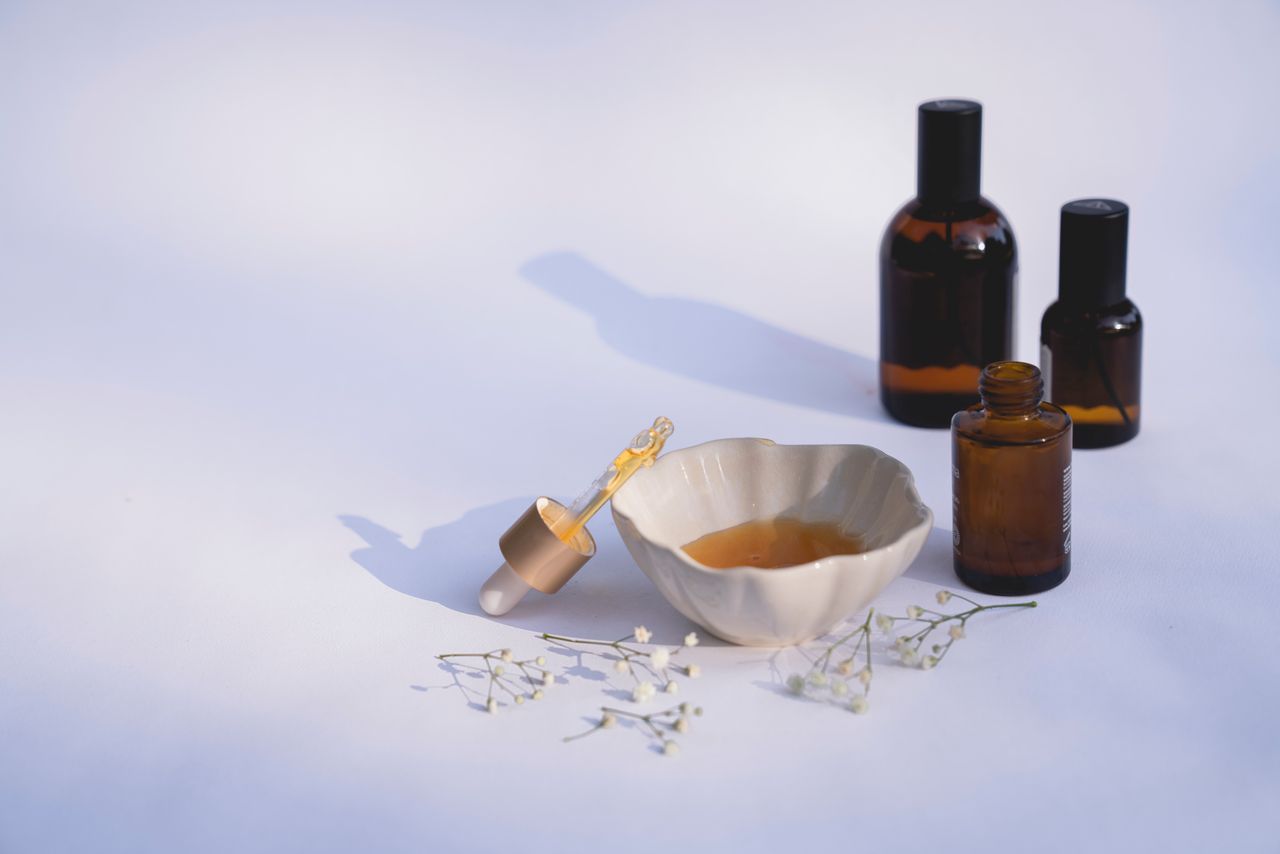 services-02 Elegant minimalistic display of amber glass bottles, ceramic bowl, dropper, and flowers on white background.